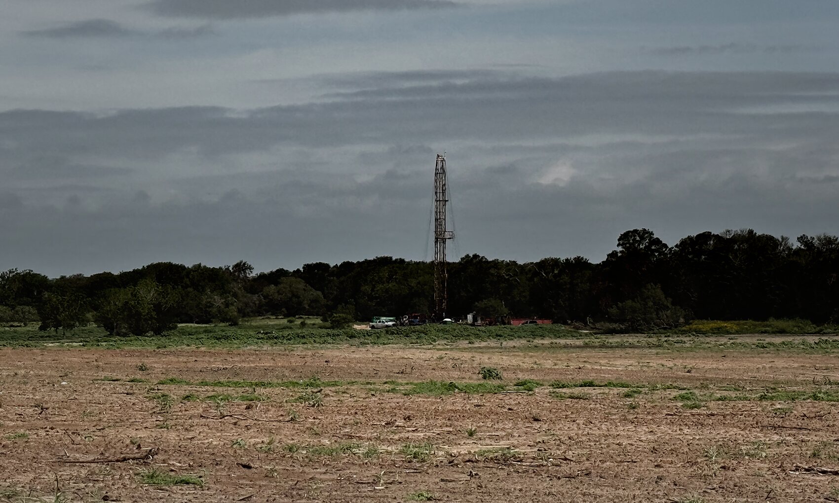 Drilling rig on the treeline horizon across open ranch land in Gonzales County, Texas